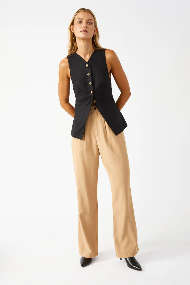Woman wearing a black sleeveless vest over a beige top and pants on a white background