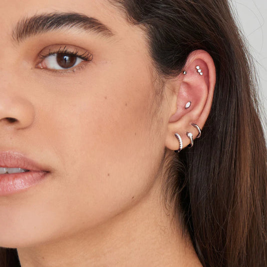Close-up of a woman's ear with multiple earrings against a neutral background