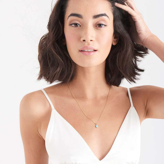 Woman wearing a white top and gold necklace with a blue pendant on a light background