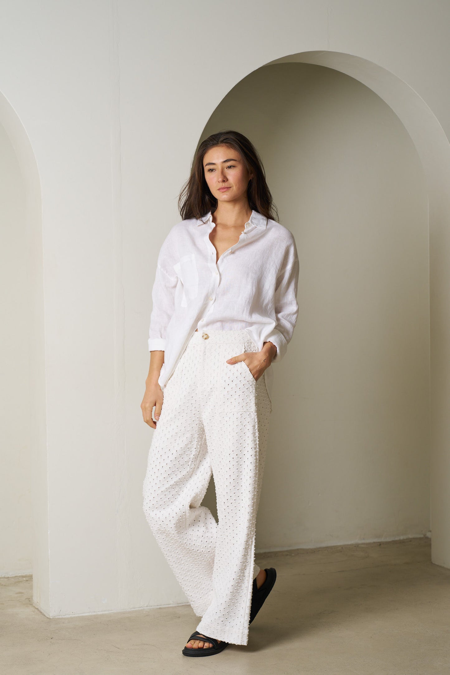 Woman wearing a white outfit standing in a minimalistic room with a white archway.